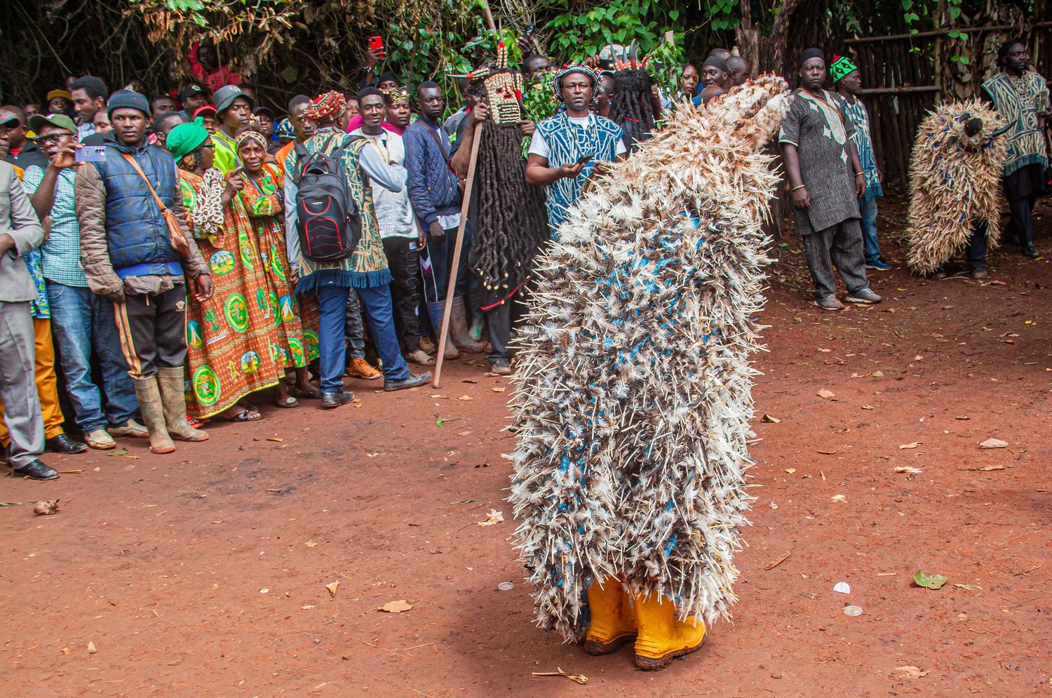 Traditional African dancer in elaborate grass costume performing before a crowd at a cultural festival.