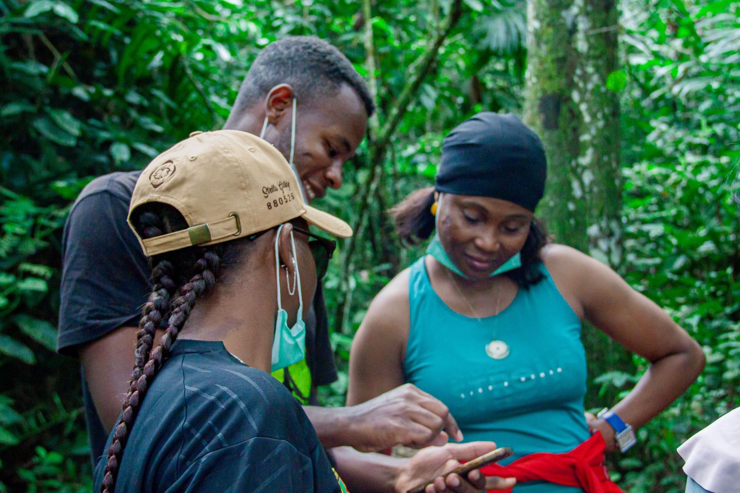 Two people examining something together in a lush tropical rainforest while wearing face masks outdoors.