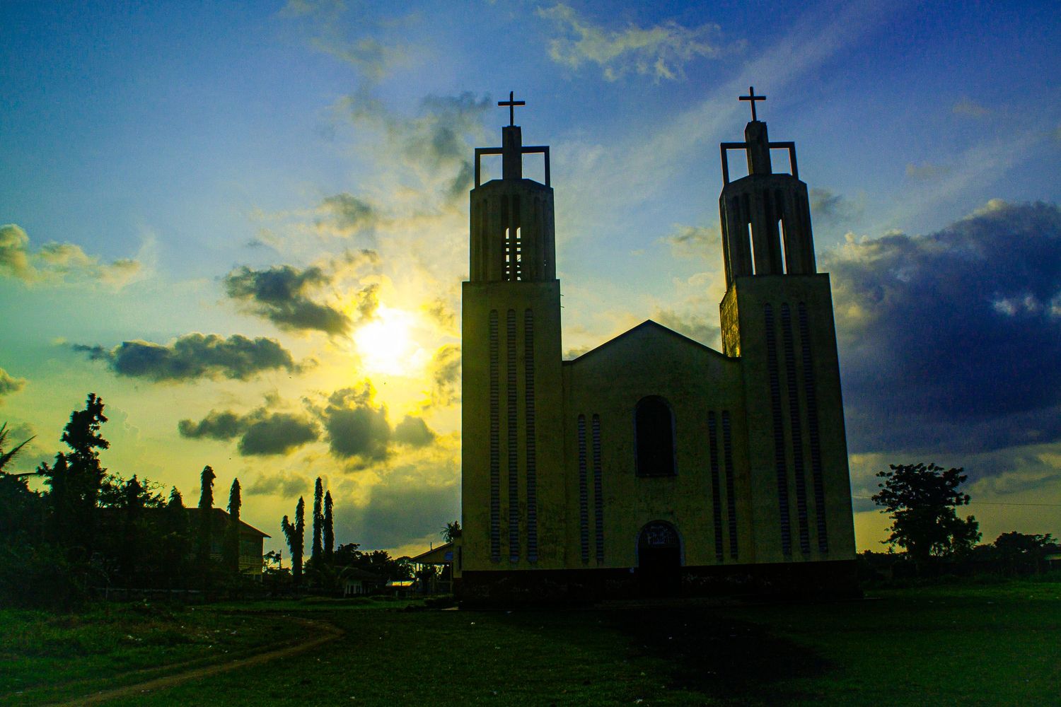 Silhouette of a twin-tower church with crosses against a dramatic sunset sky with golden clouds.