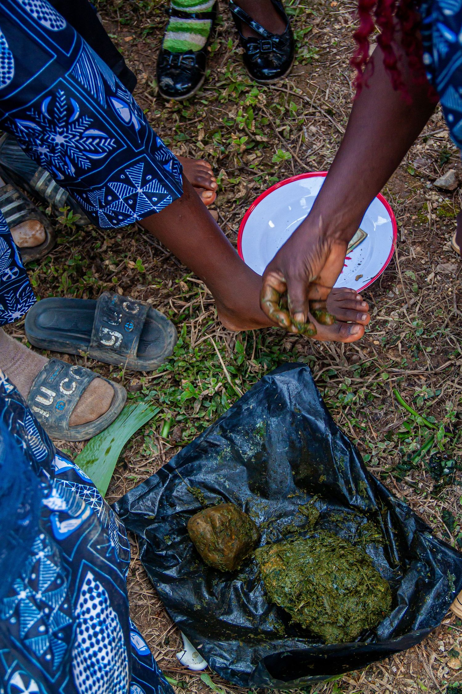 Hands preparing traditional African food with green-coated yams in a black bag outdoors.