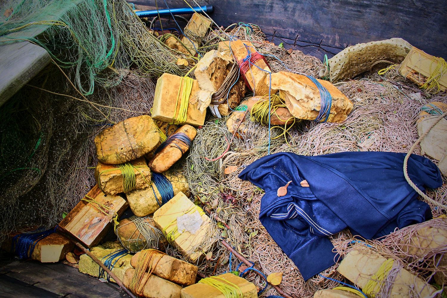 Yellow buoys, rope, and a blue bag lie tangled in green fishing nets inside a wooden boat.