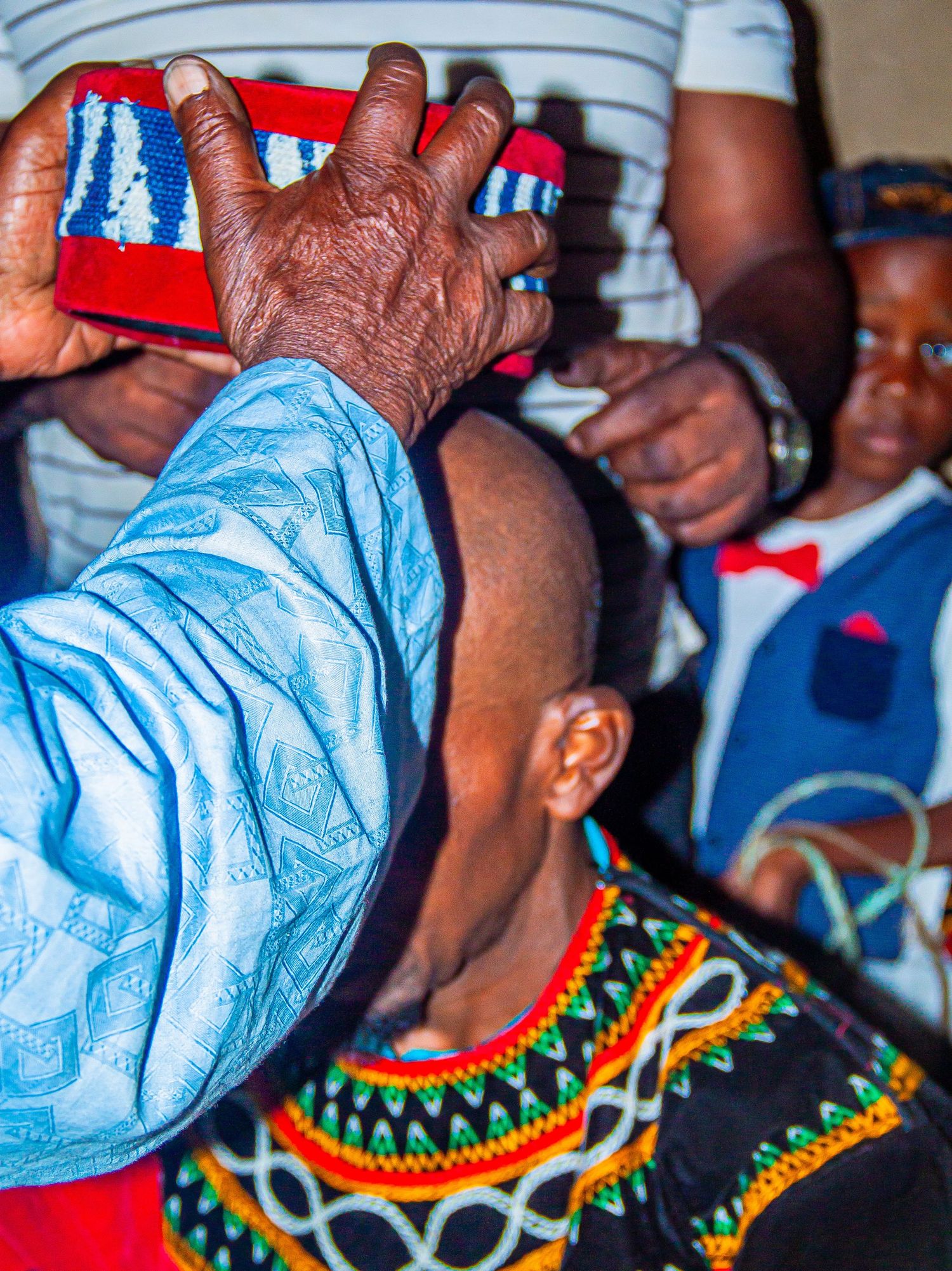An elder places a colorful beaded crown on a person wearing traditional African embroidered attire.