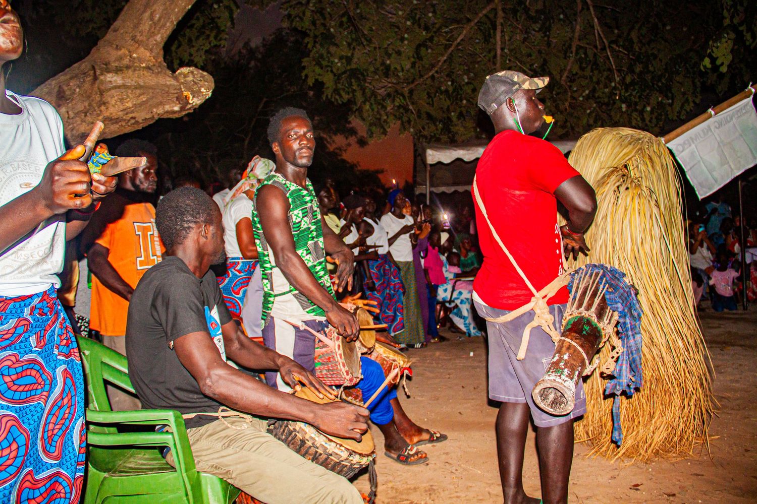 Traditional African cultural ceremony with musicians and dancers performing outdoors at night.