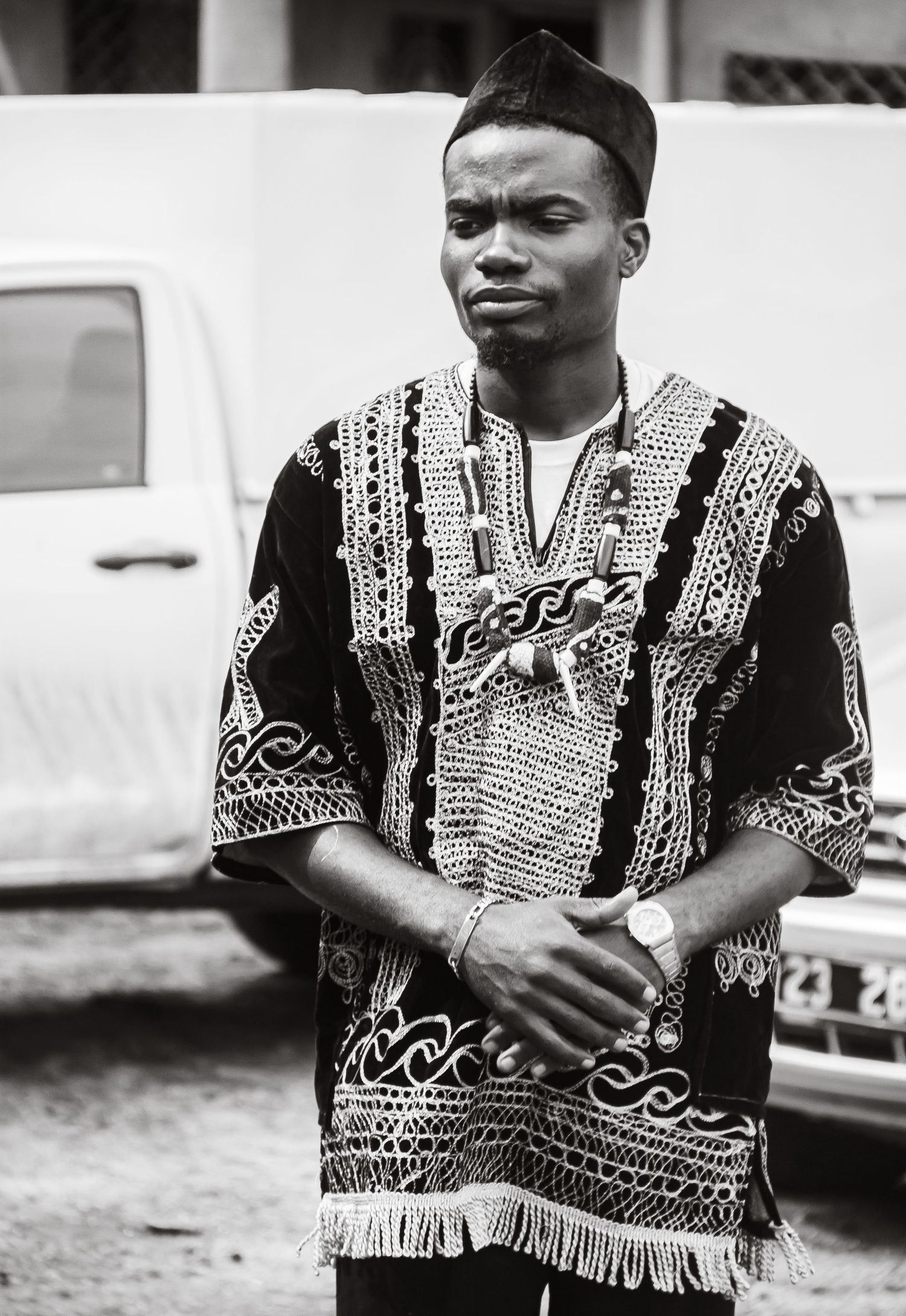 A black and white portrait of a young African man in traditional embroidered attire with a watch.