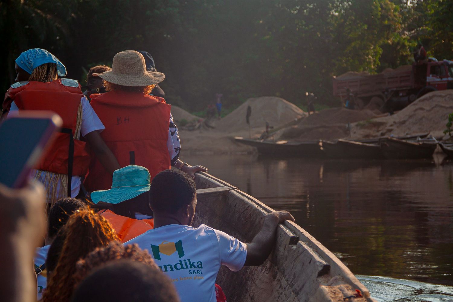 Group of people riding in wooden boat on calm river at golden sunset hour.