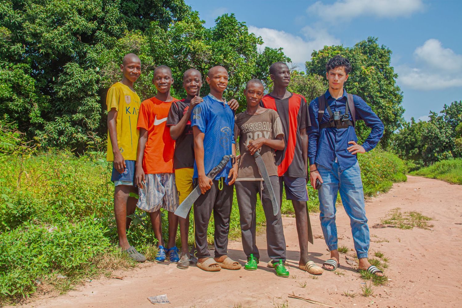 Group of seven young African men and one tourist posing on a rural dirt road.