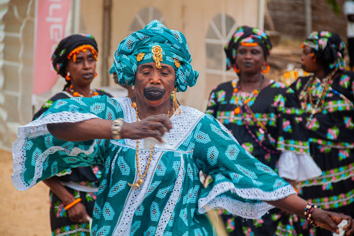 A woman in teal traditional African dress performs a cultural dance at an outdoor event.