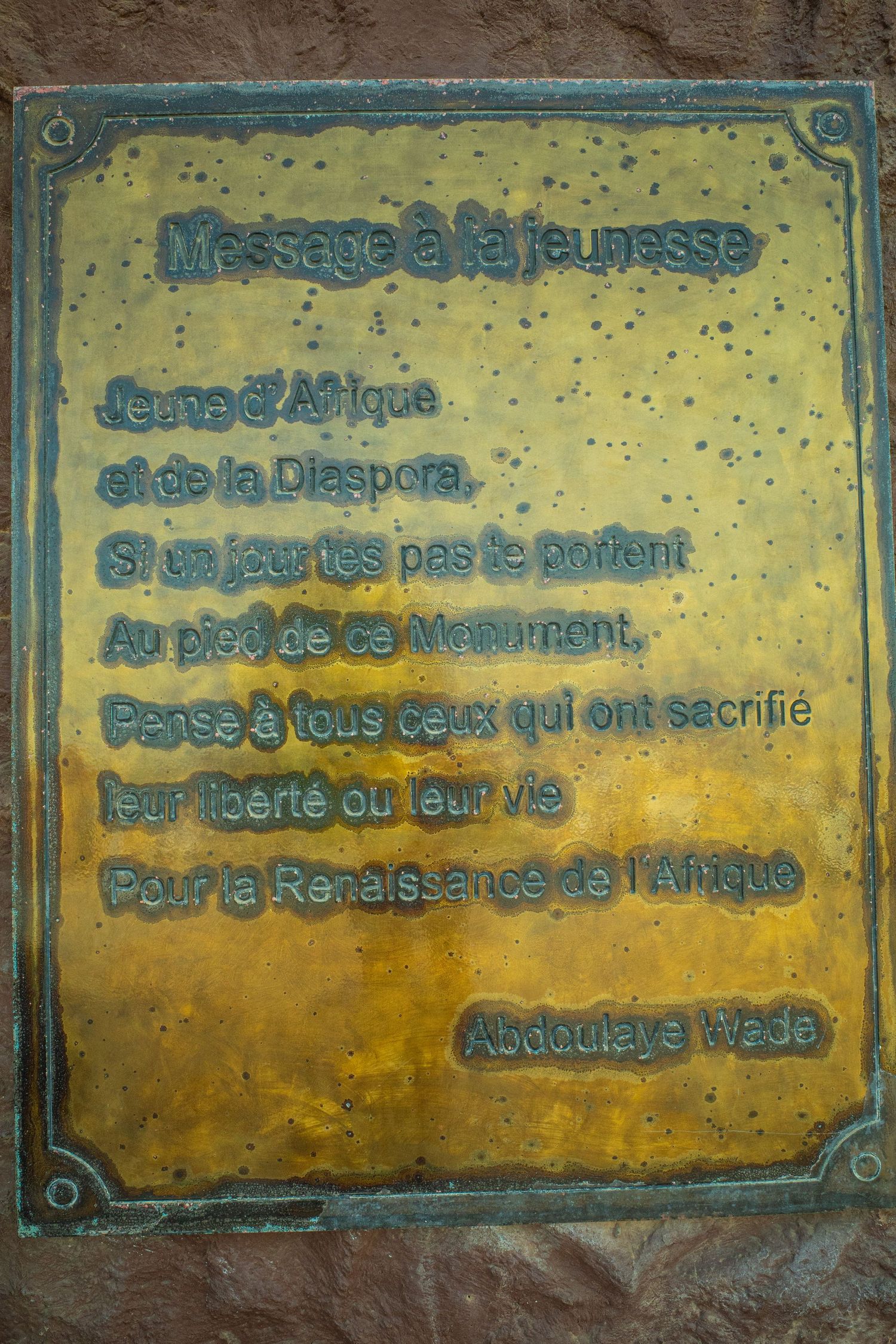Brass plaque with French poem titled Massage a la Jeunesse signed by Abdoulaye Wade on stone monument.