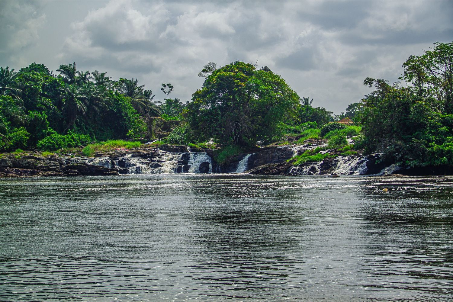 Scenic tropical waterfall cascading over rocks into a calm river surrounded by palm trees.