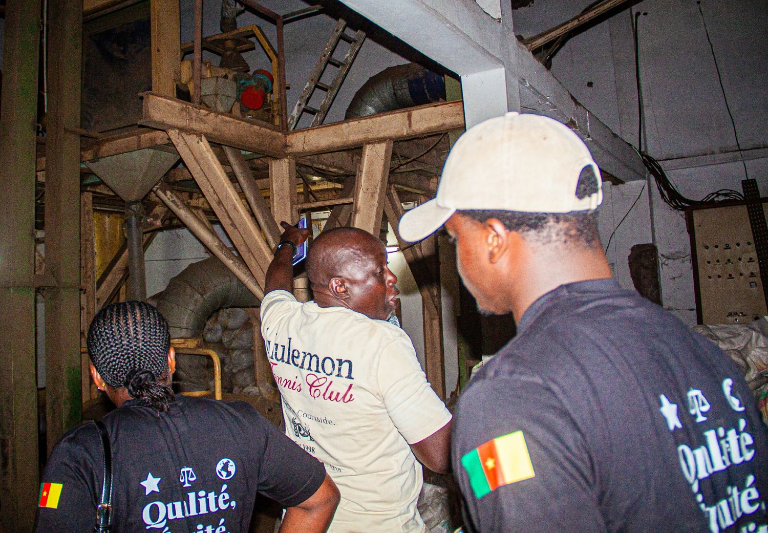 Workers in matching black shirts inspecting industrial machinery inside a food processing facility.