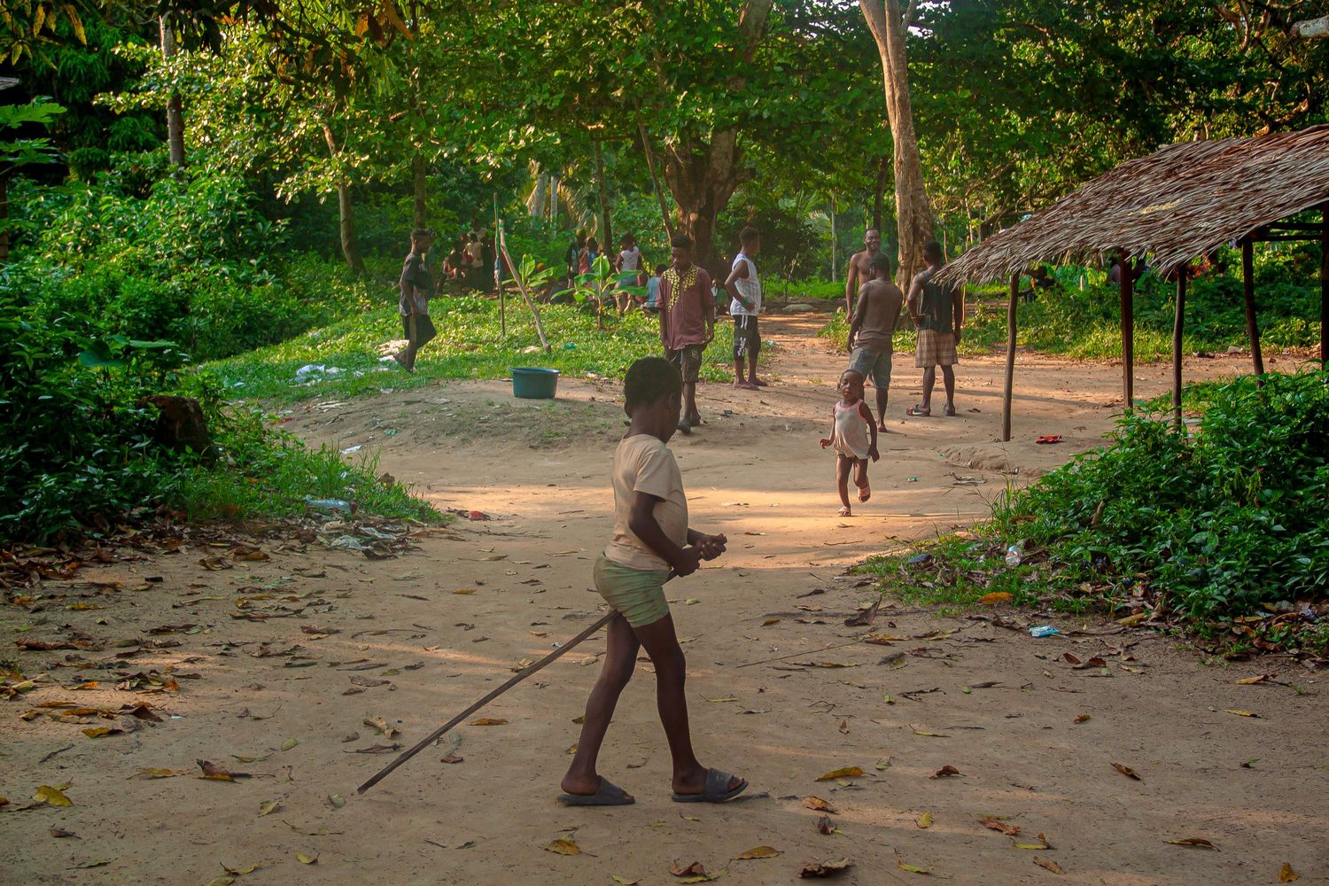 African children playing in sandy village path surrounded by lush tropical green trees.