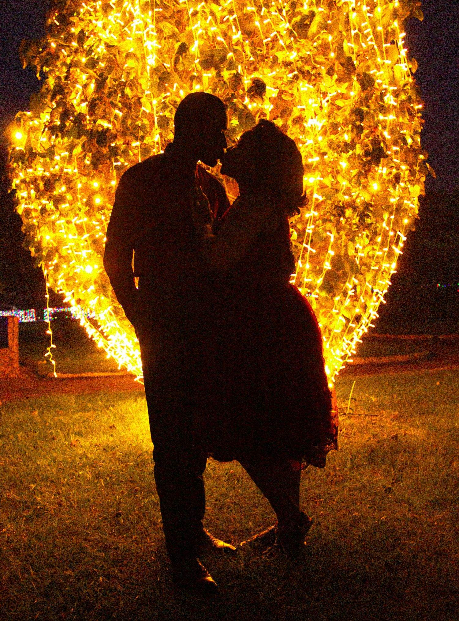 Romantic couple silhouette kissing in front of glowing heart-shaped light display at night.