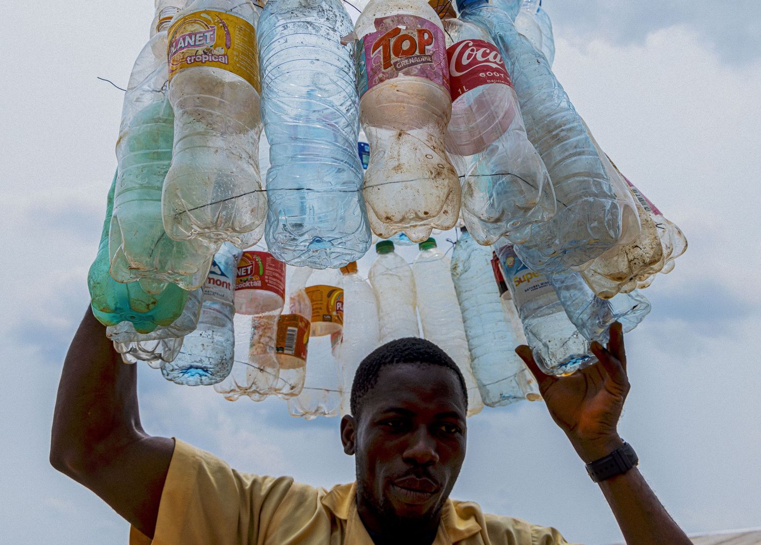 African street vendor balancing a large bundle of plastic bottles on his head outdoors.