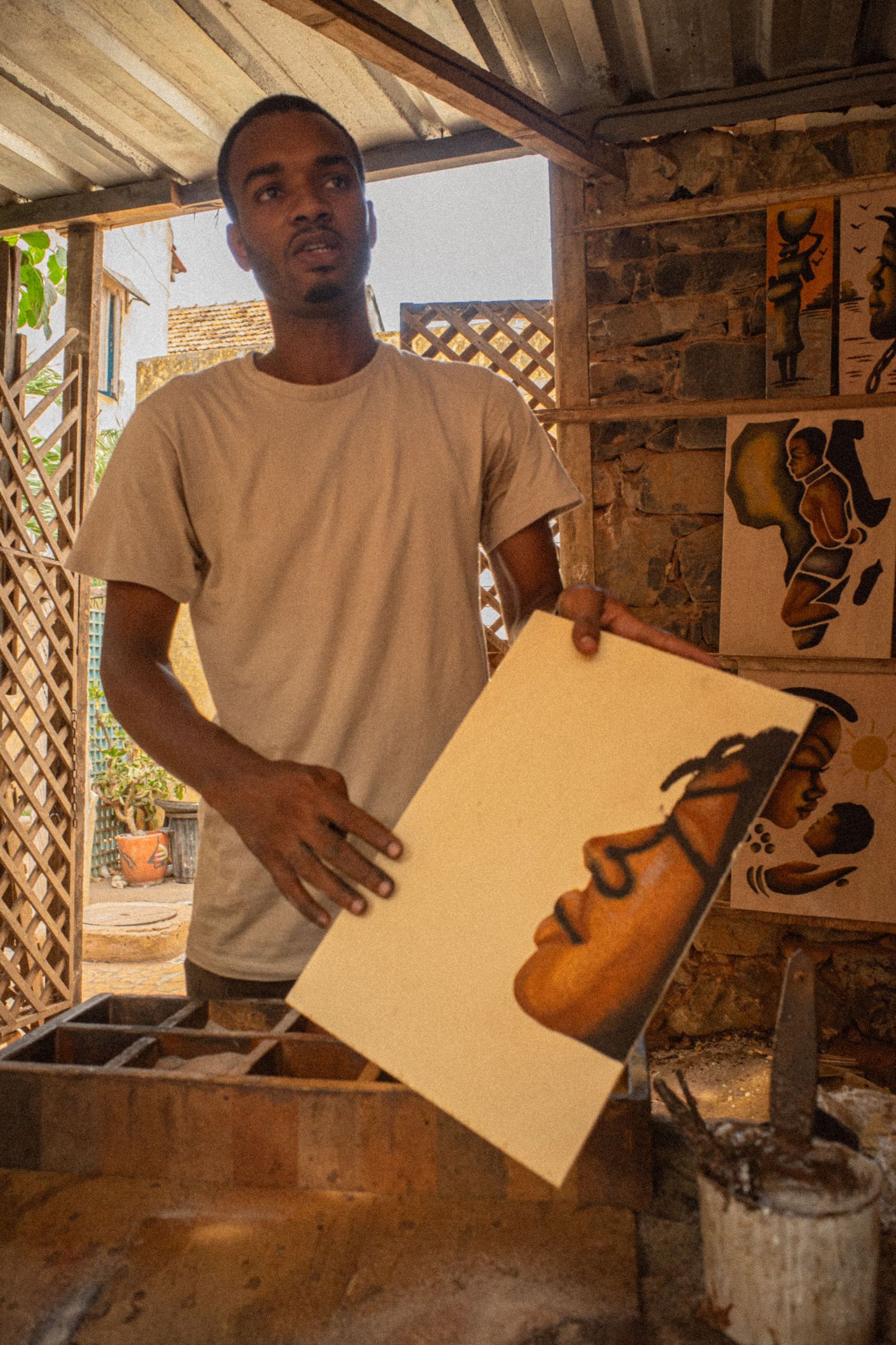 A young African artist proudly displays a portrait painting in his rustic studio workshop.