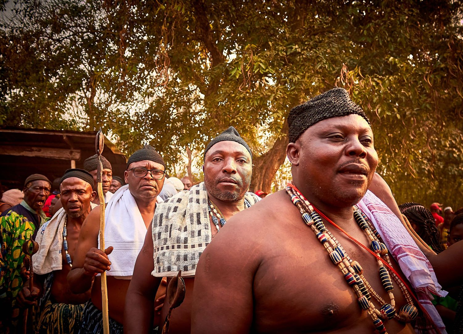 Traditional African tribal leaders in ceremonial beaded attire gathered outdoors during a cultural ceremony at sunset.