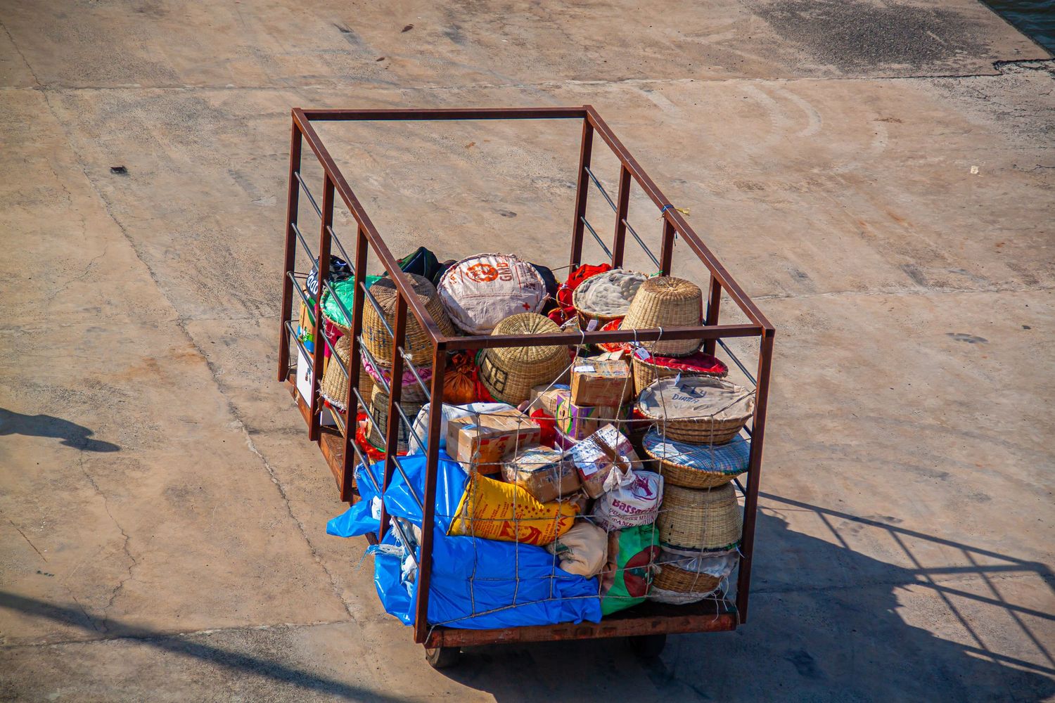 Overhead view of a metal cage cart loaded with colorful bags and goods on pavement.