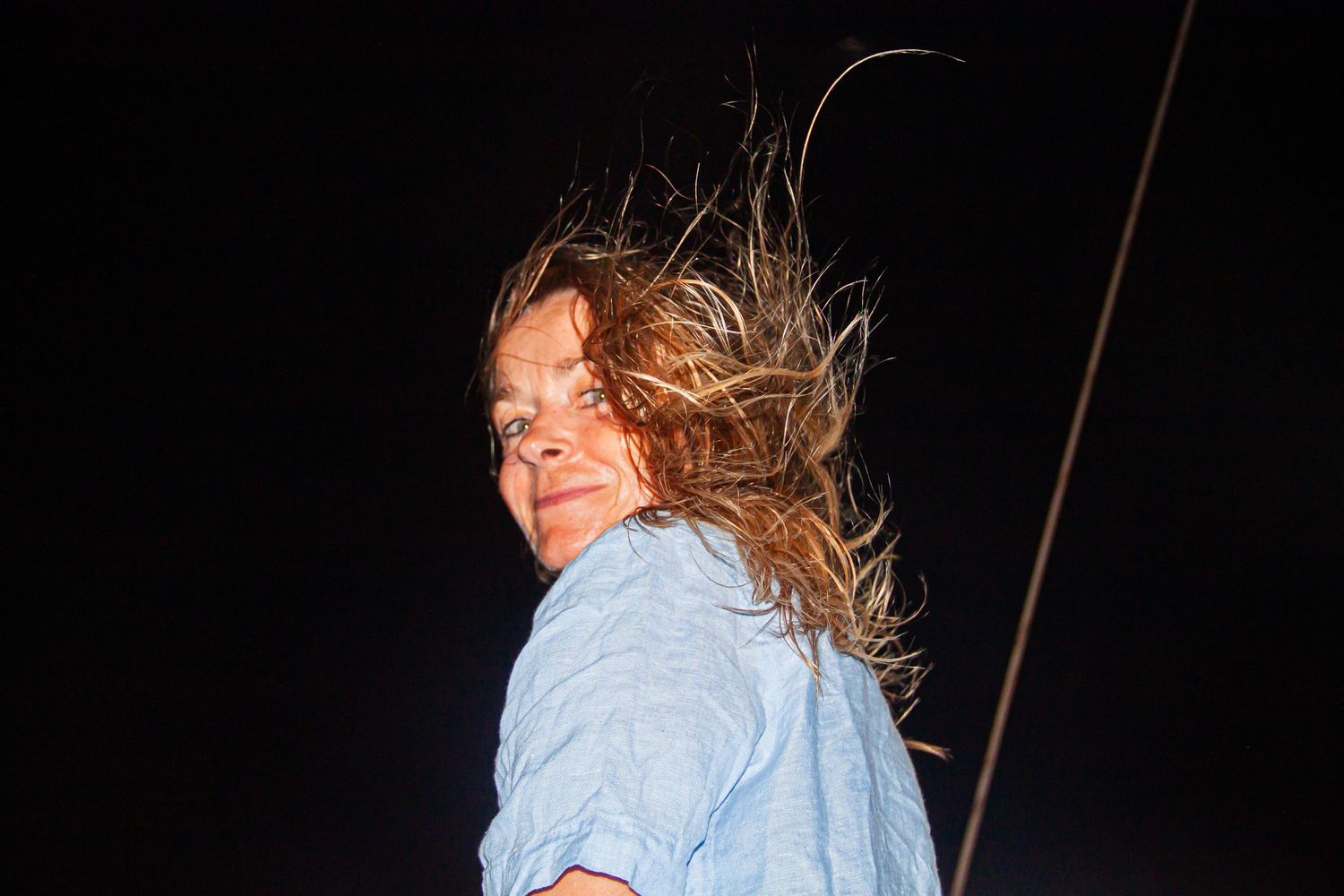 Woman with windswept hair looking back over her shoulder against a dark night sky.