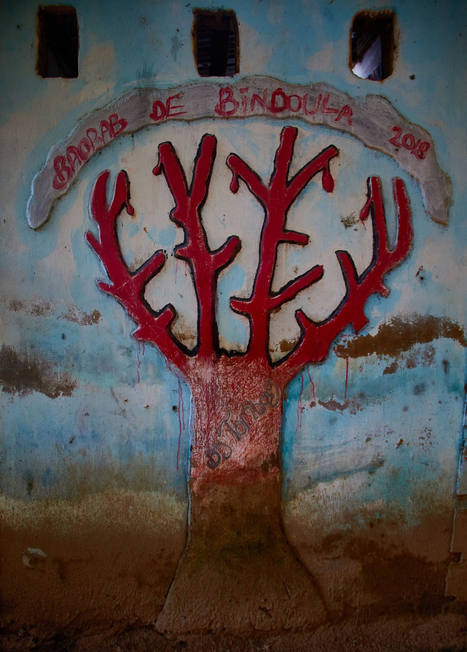 Colorful mural of a red baobab tree painted on a weathered blue wall.