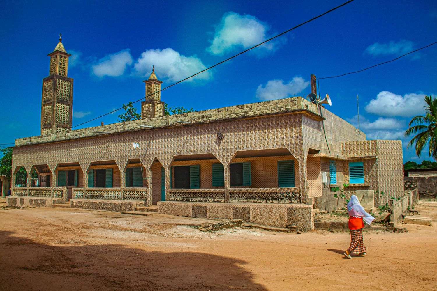 Colorful mosque with ornate facade and tall minaret on a dusty road in a West African town.