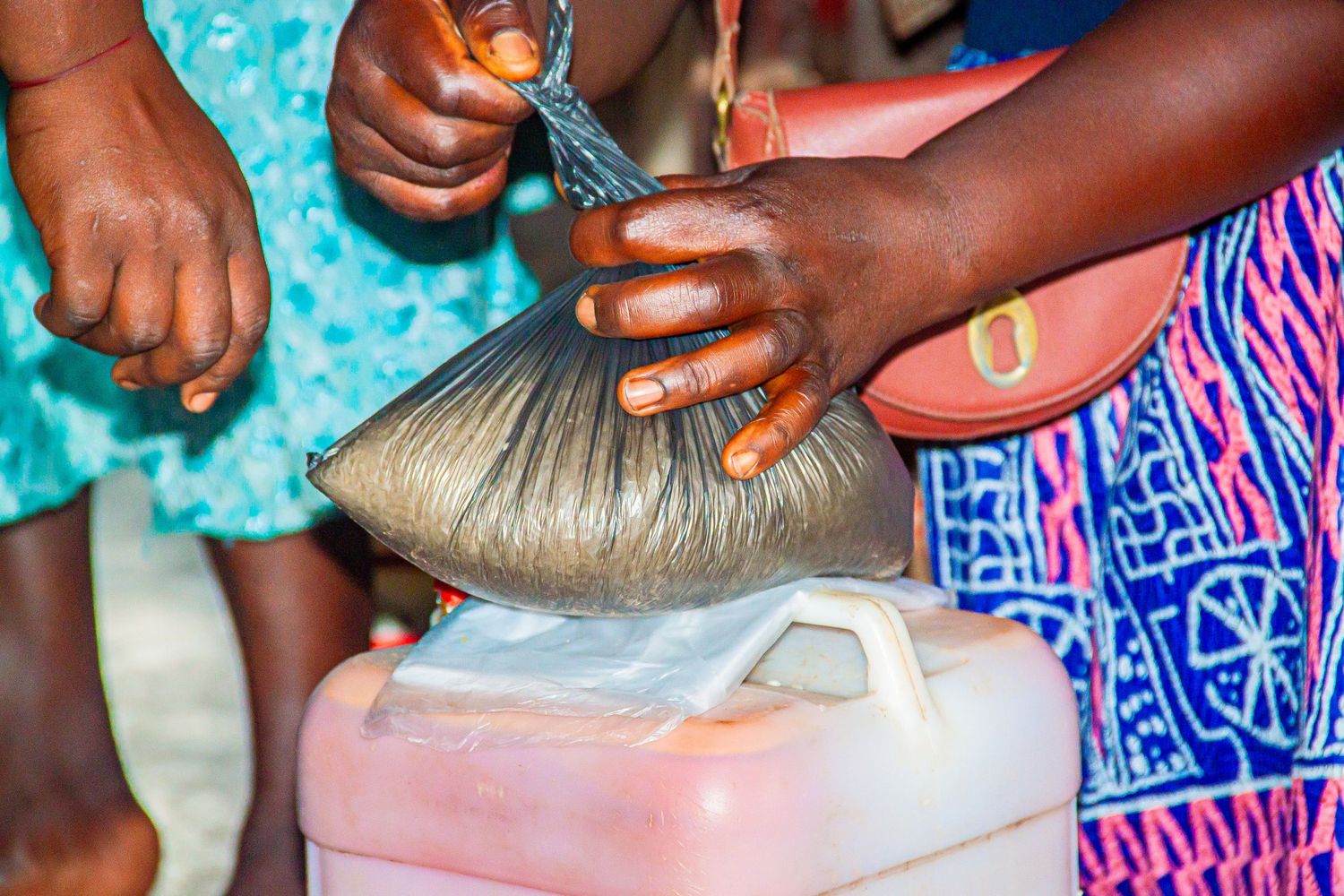 African women pouring grain from a plastic bag into a jerry can at a local food distribution point.