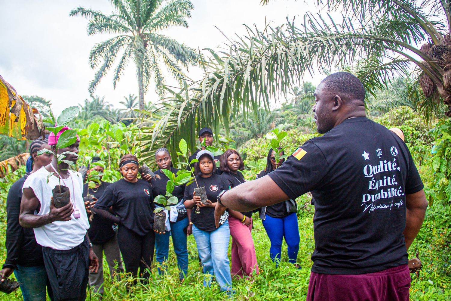 Agricultural trainer in black shirt presenting seedlings to a group of farmers in a tropical farm.