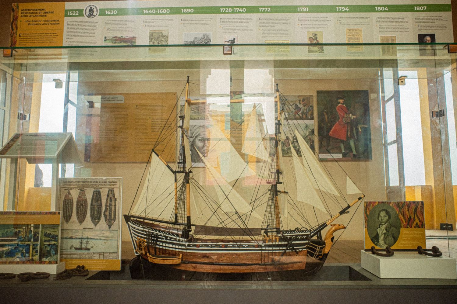 Historic sailing ship model displayed in a museum glass case with maritime artifacts.