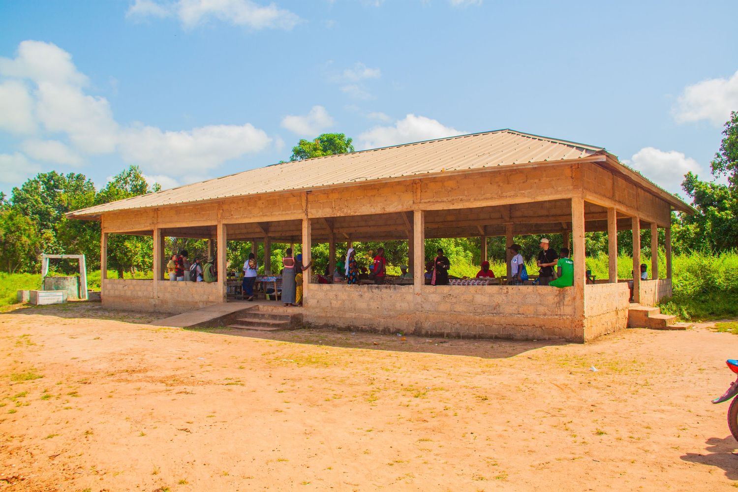 Open-air community building with people gathered inside surrounded by lush greenery in Africa.