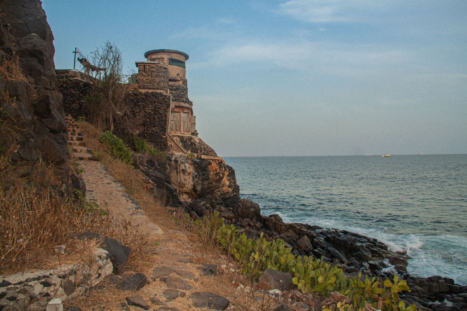 Narrow rocky coastal path leading to a historic stone watchtower on dramatic cliffs above the Atlantic Ocean.