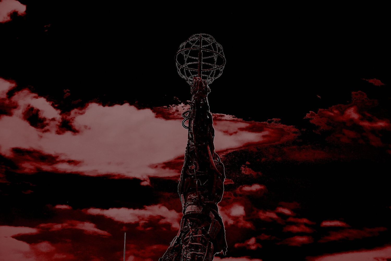 Dramatic red sky silhouettes a globe sculpture atop a tall monument at dusk.