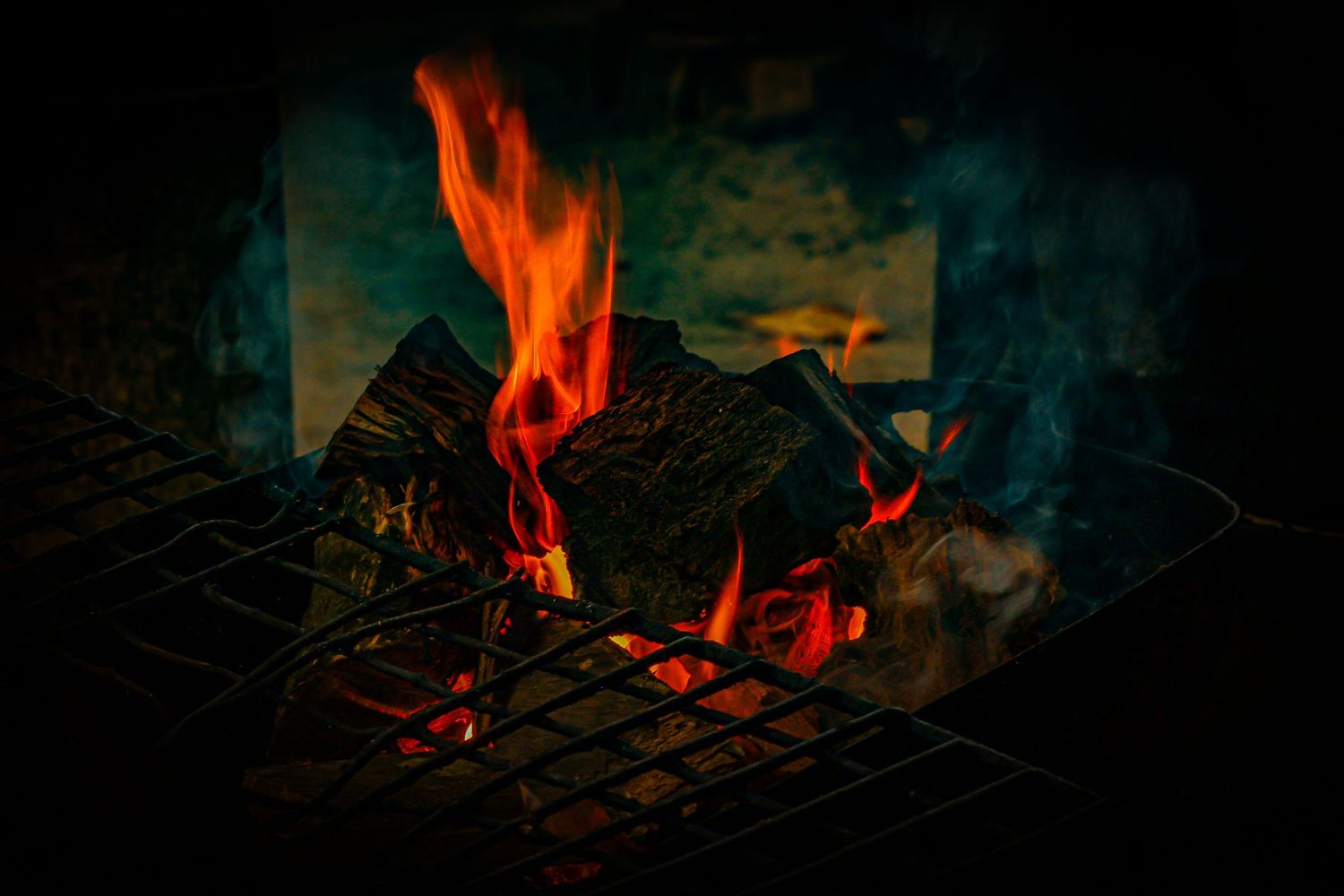Bright orange flames burning wood logs on a dark metal grill in a fireplace.
