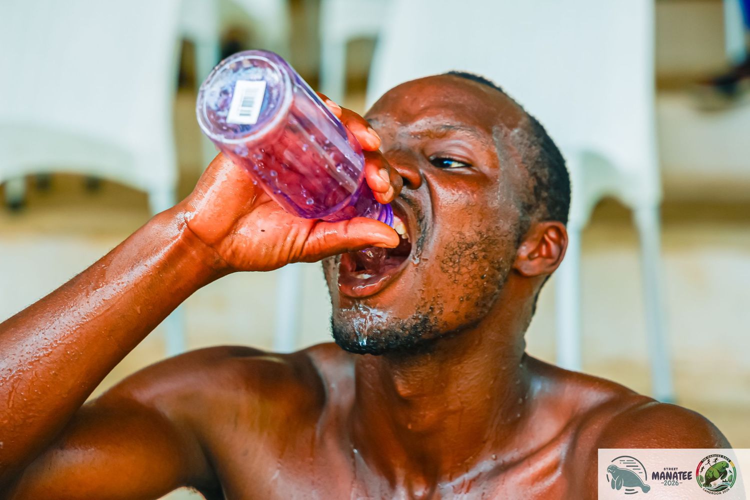 Exhausted male athlete drinking from plastic bottle after intense workout outdoors.