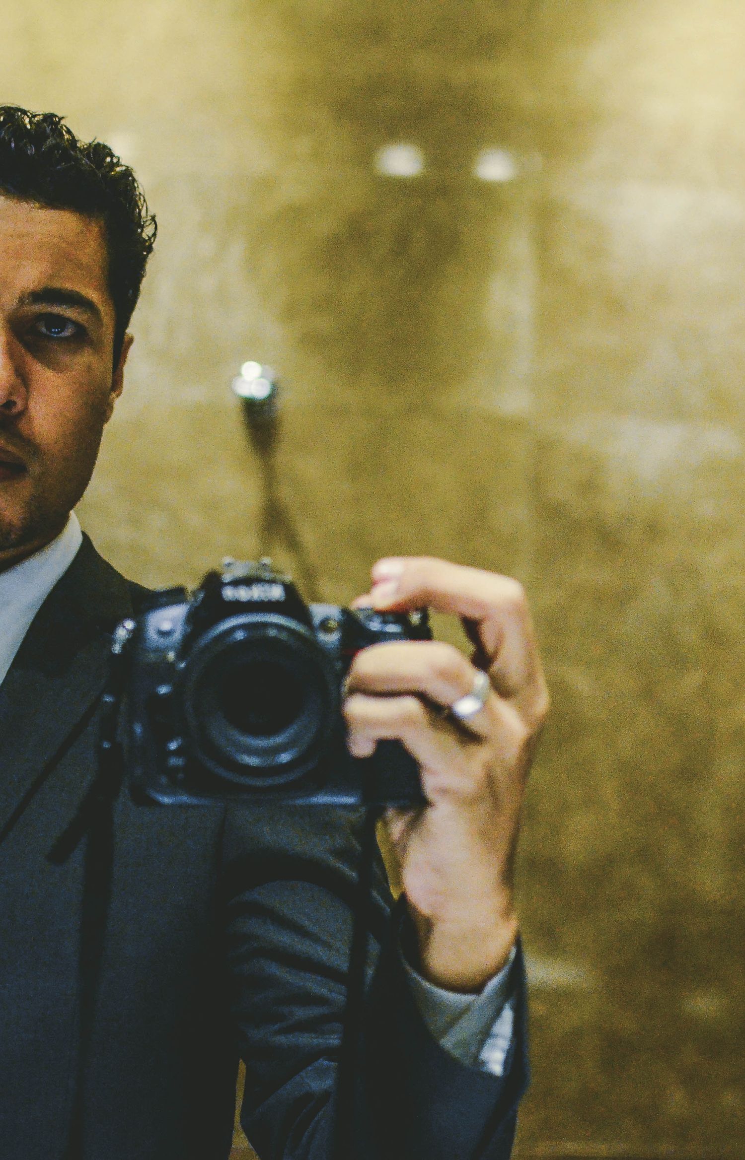 Professional fine art photographer M Kazzaz self portrait mirror shot holding a premium Nikon camera body inside studio.