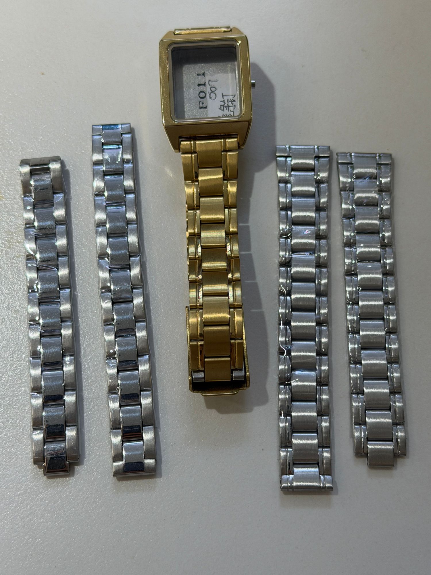 Gold-tone watch with multiple silver and two-tone replacement metal bracelet bands laid flat.