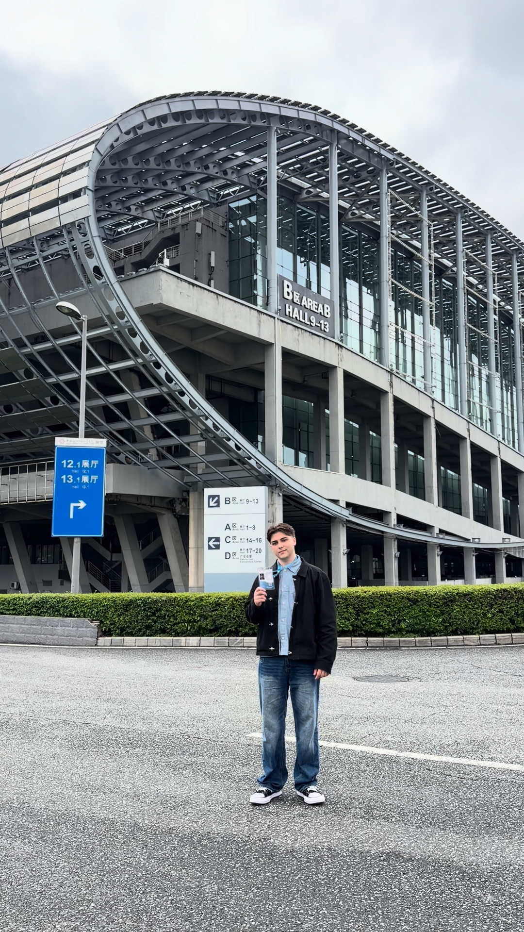 Young man standing in front of a modern curved glass convention center building with Japanese signage.
