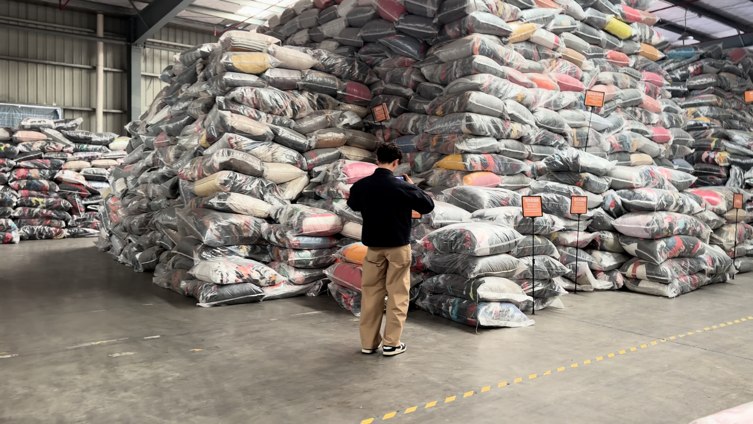 Person standing in front of massive stacks of large bundled fabric bags in a warehouse.