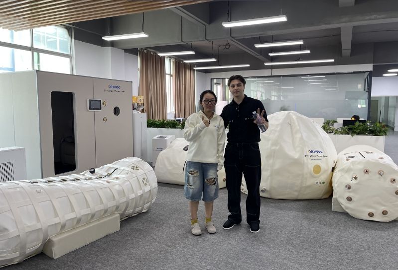 Two people posing beside large white hyperbaric oxygen chambers in a modern medical showroom.