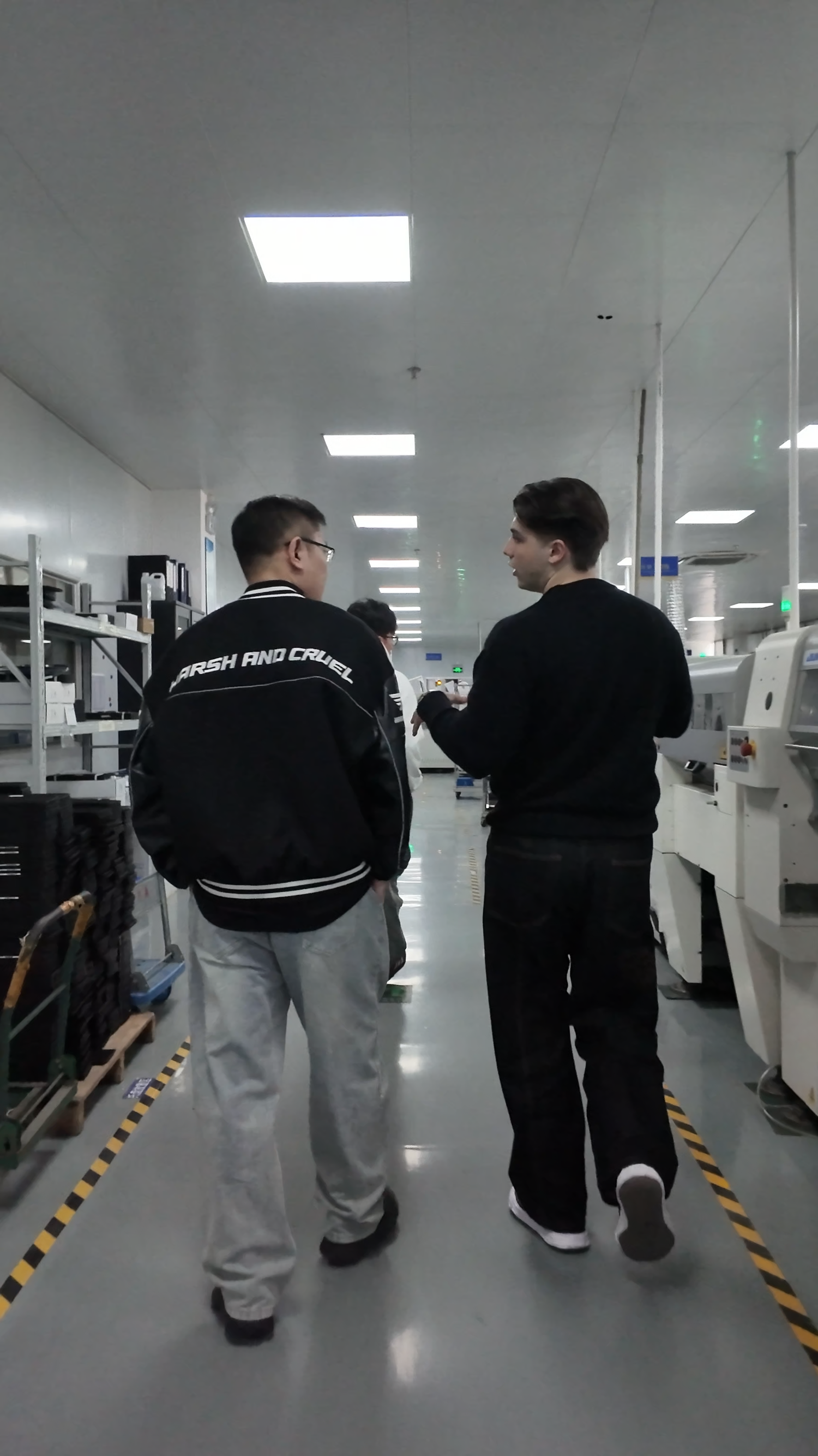Two men walking through a bright electronics manufacturing facility with machinery.