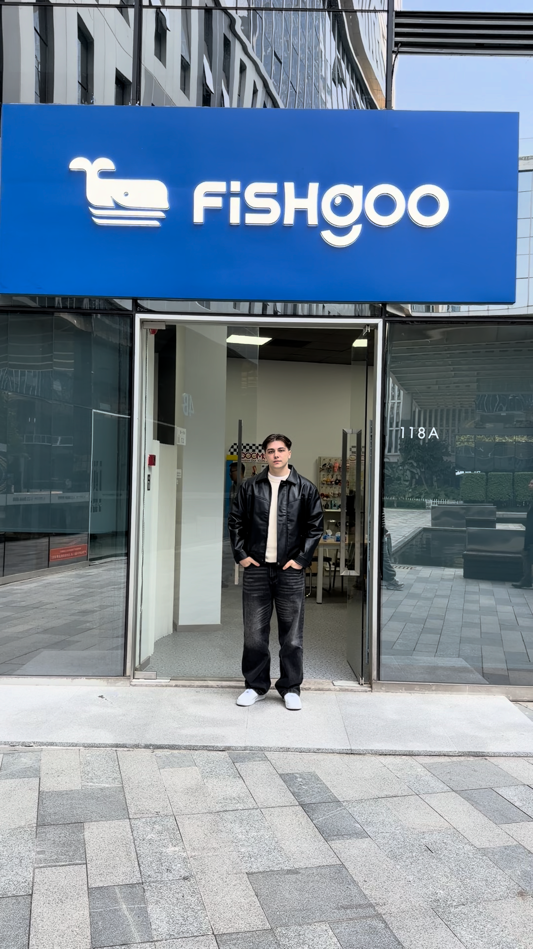 Man in black jacket stands outside Fishgoo store entrance with blue signage and whale logo.
