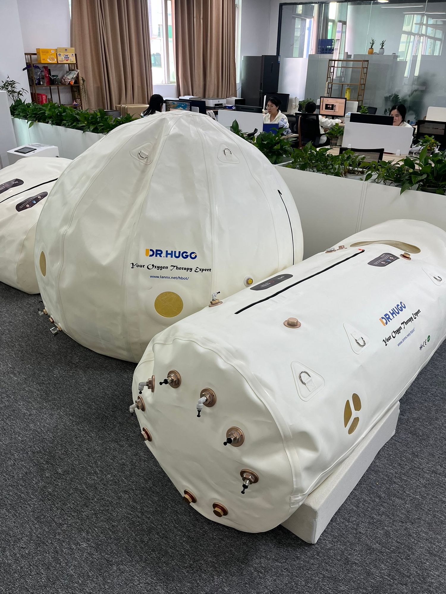Two white DR HUGG hyperbaric oxygen therapy chambers displayed in a modern office setting.