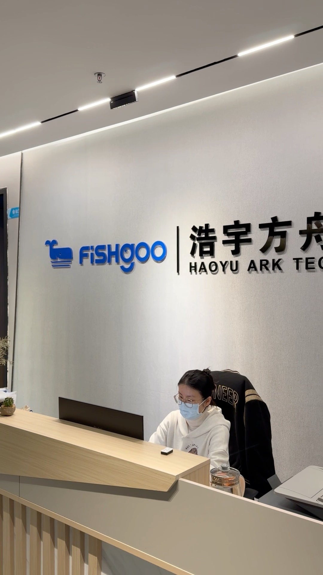A masked receptionist sits at the front desk of Fishgoo Haoyu Ark Technology office in China.