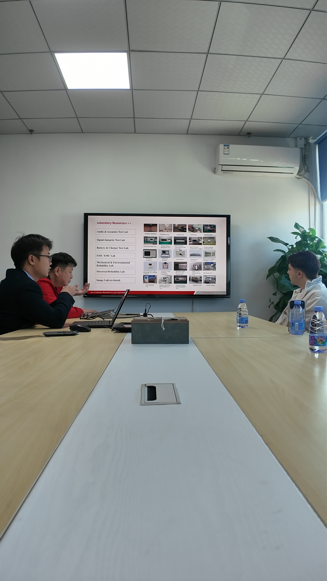 Business professionals in a conference room viewing a presentation on a large display screen with a laptop.