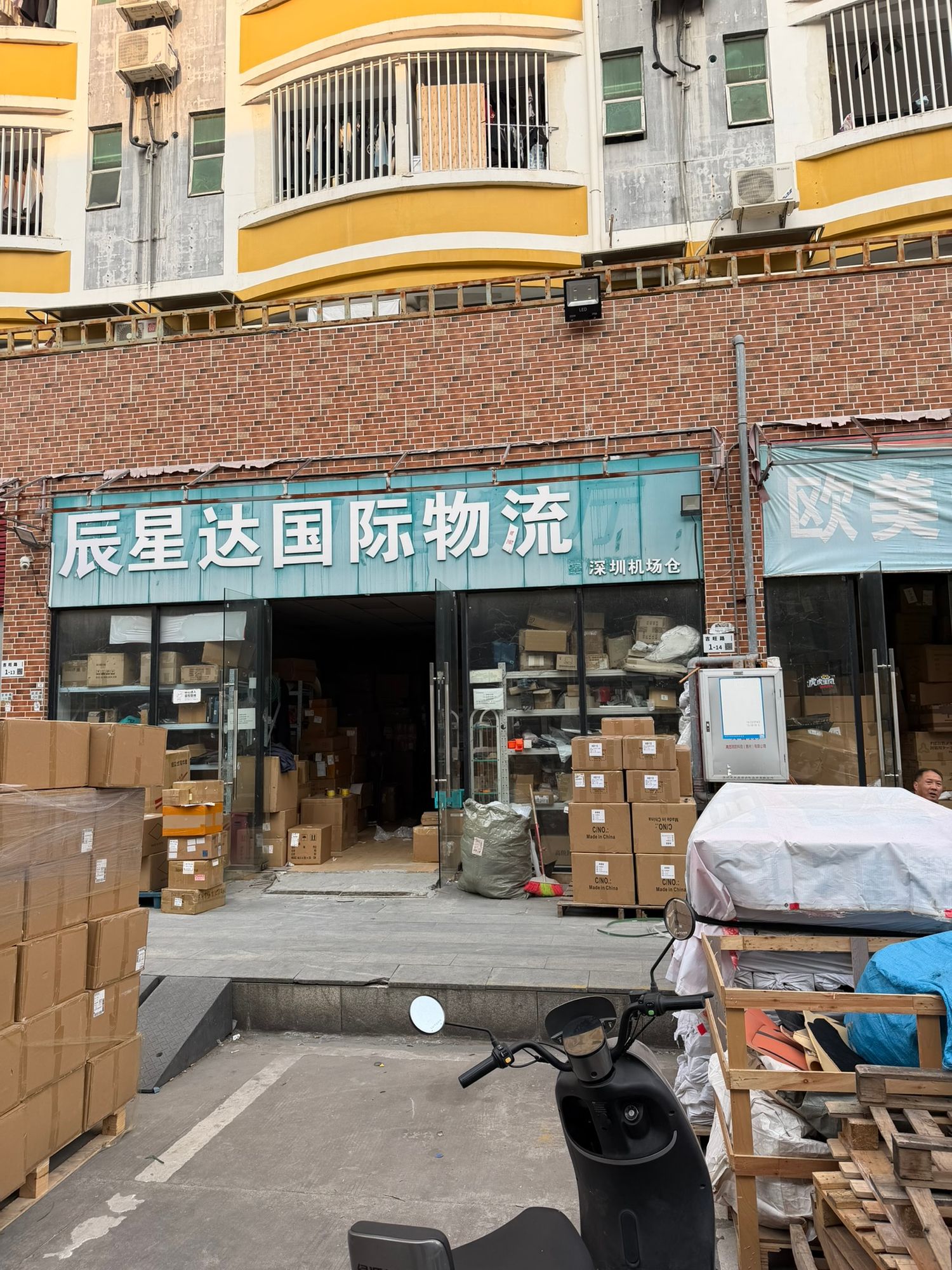 Chinese international logistics company storefront with boxes and packages visible inside a brick building.