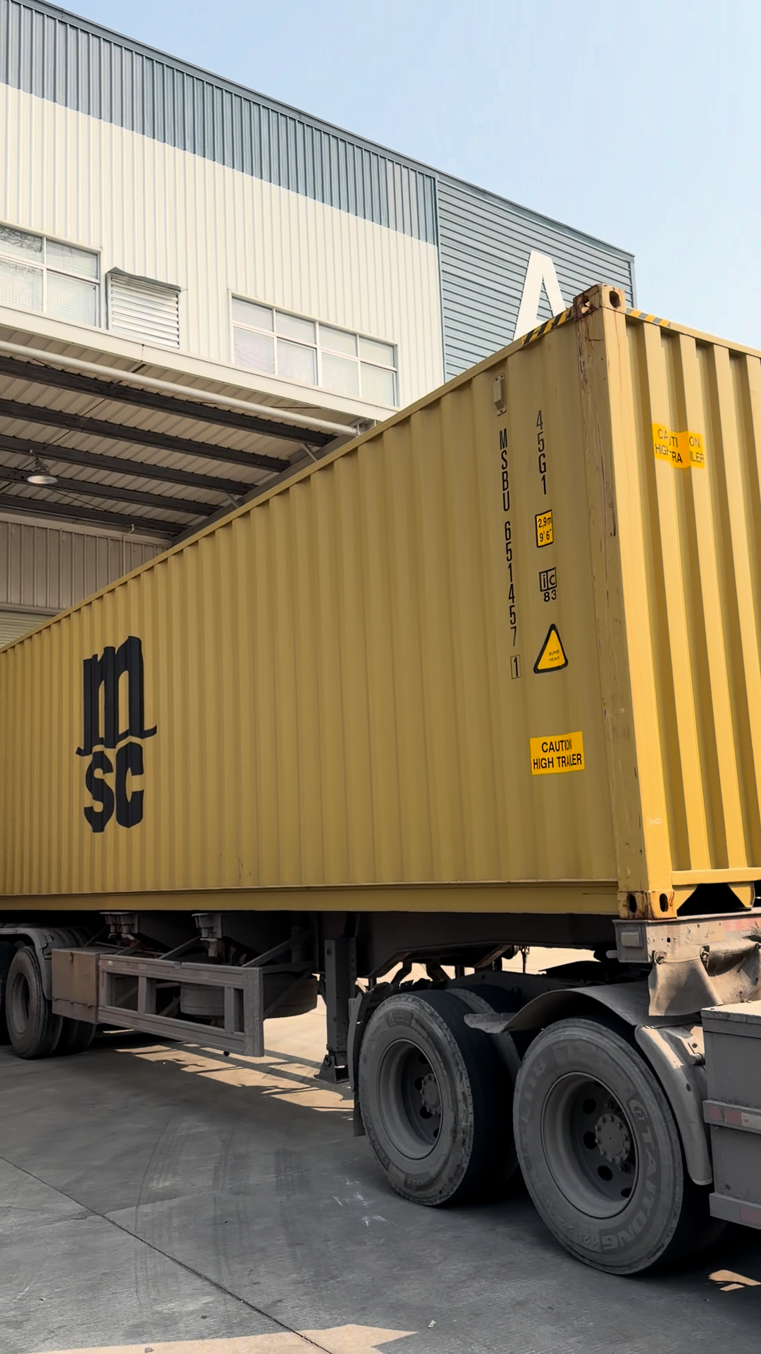 MSC yellow shipping container on a semi-truck trailer parked at an industrial warehouse loading dock.