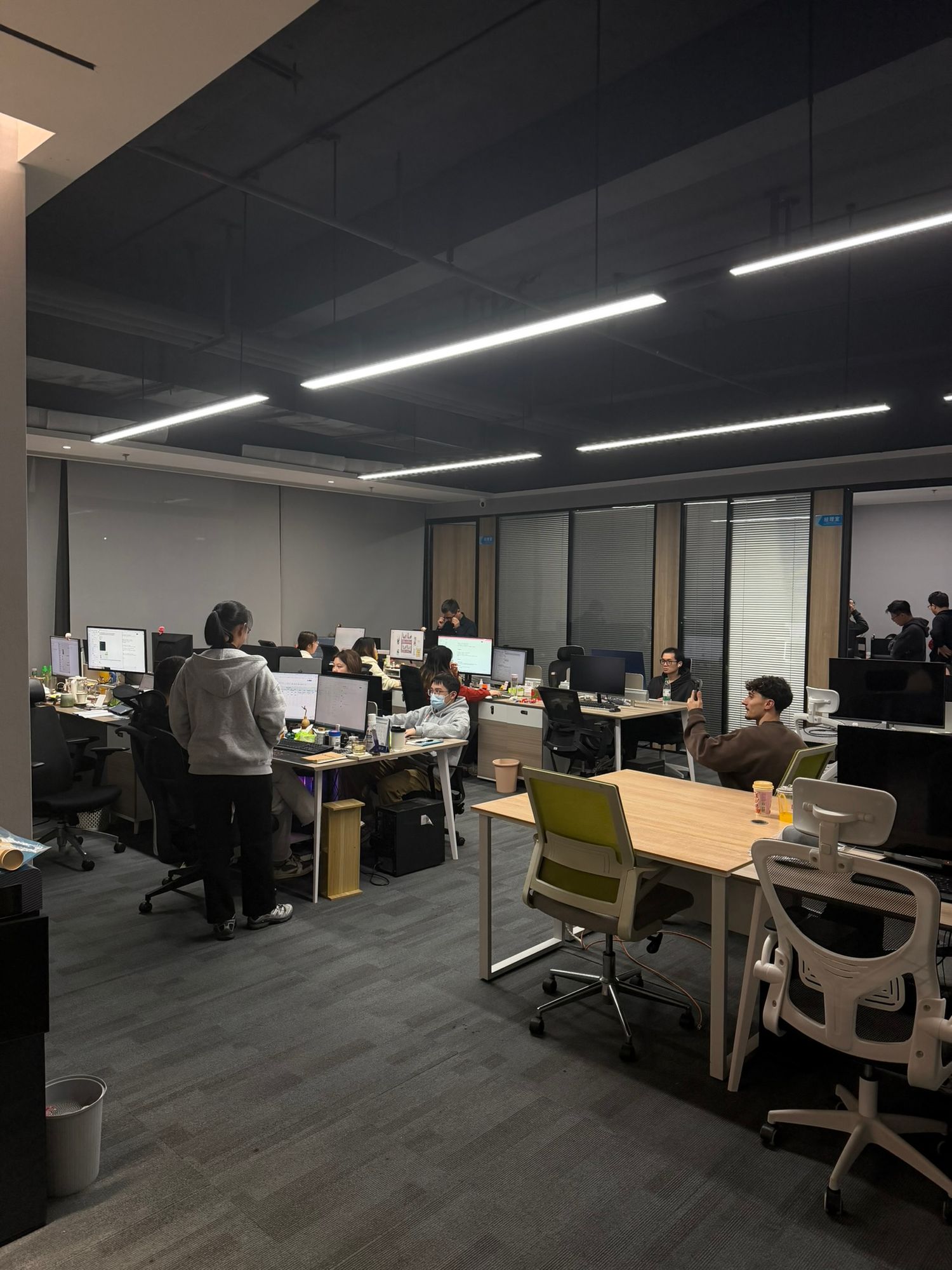 Modern open-plan office with employees working at computer desks under bright LED lighting.