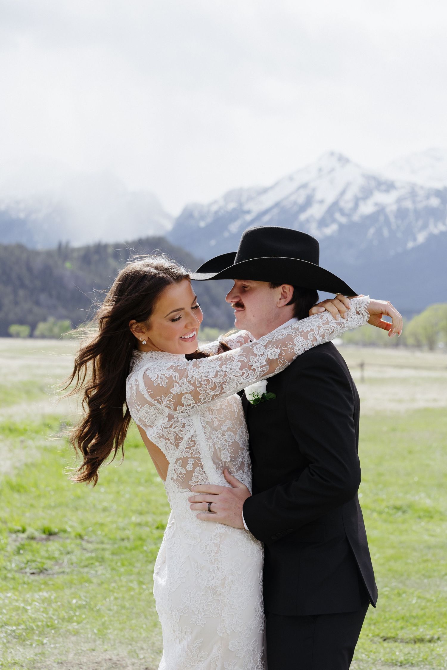 Bride and groom dancing in lace wedding dress and black cowboy hat with snowy Grand Teton mountains backdrop.