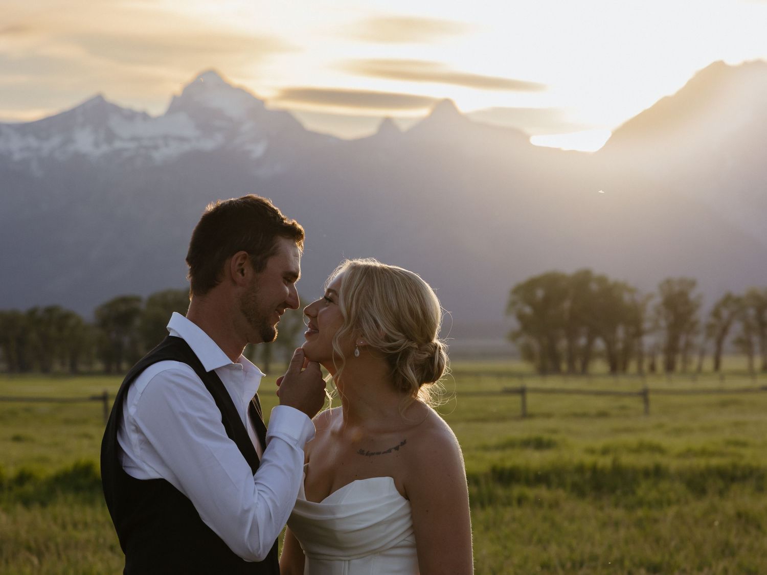Romantic couple in wedding attire embrace at golden sunset with Grand Teton mountain range glowing behind them.
