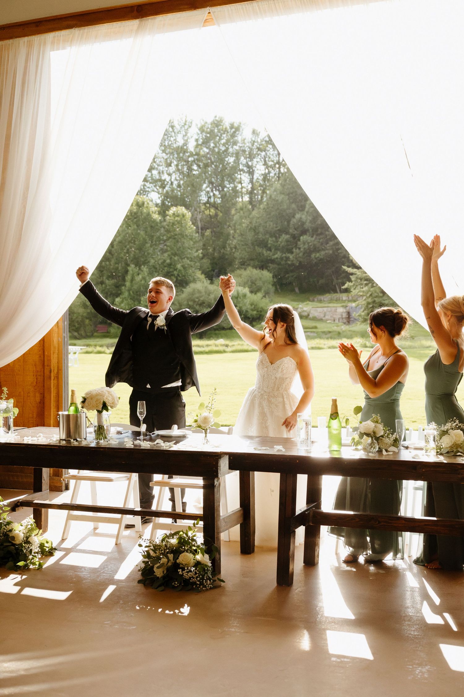 Bride and groom raise hands in celebration as they enter rustic barn reception venue.