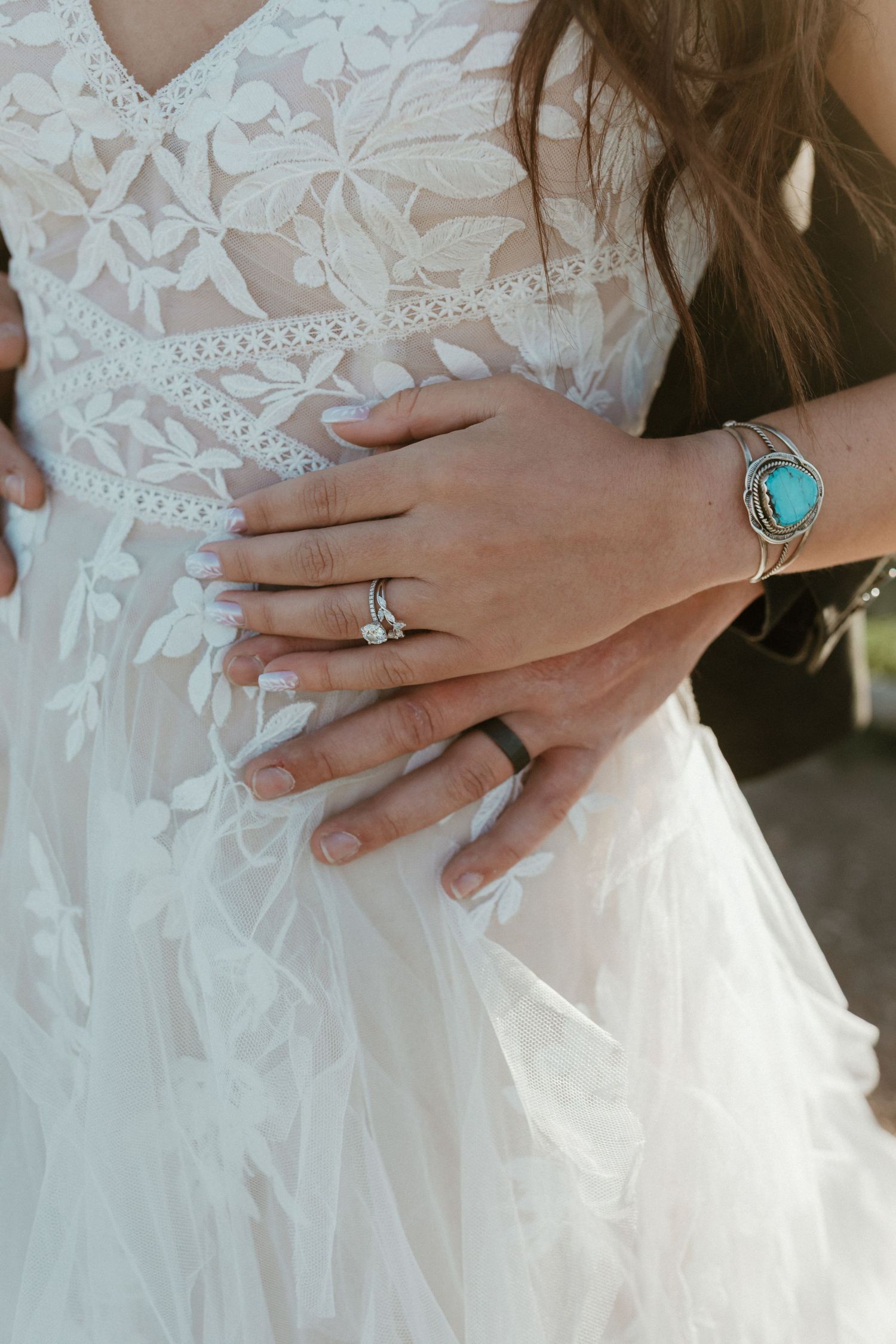 Close-up of bride and groom wedding rings, with bride wearing turquoise silver bracelet on her lace gown.
