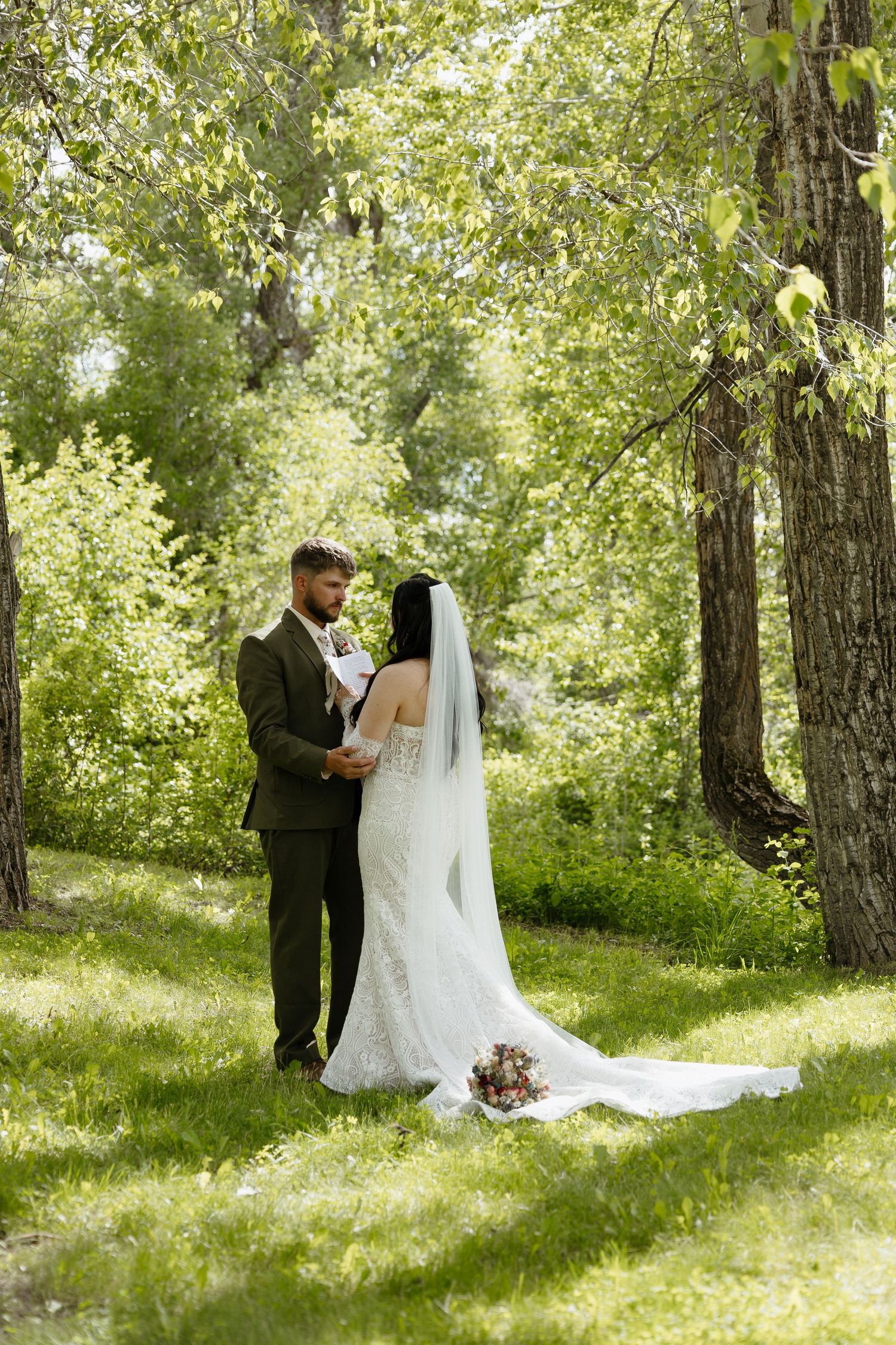 Bride and groom share an intimate moment surrounded by lush green trees at their outdoor wedding.