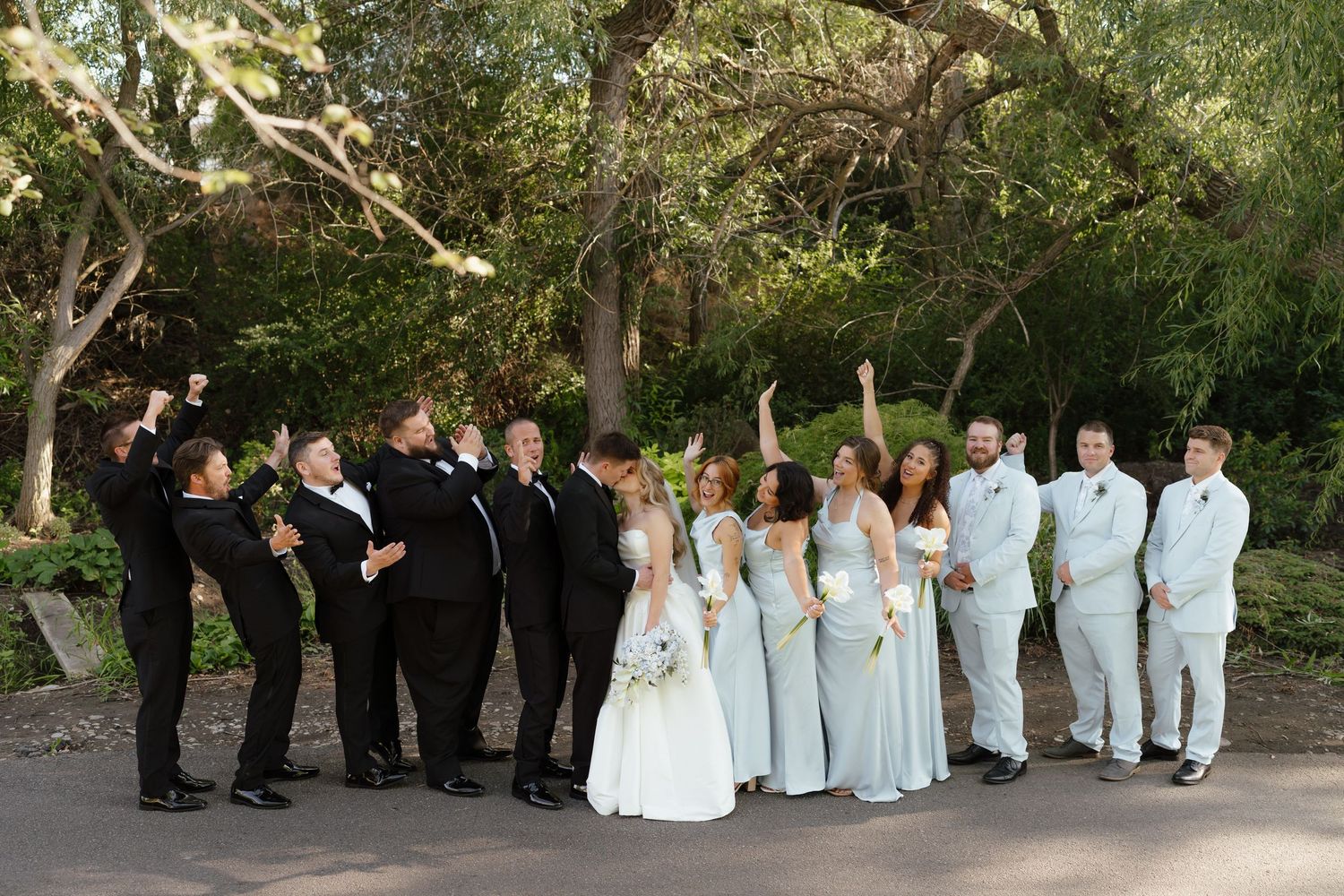 Wedding party celebrating outdoors, bride and groom with bridesmaids in mint gowns and groomsmen in black and white tuxedos.